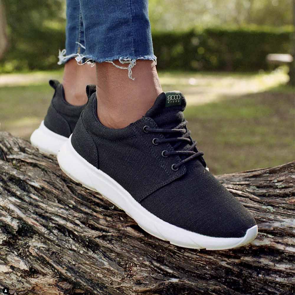 Person wearing the 8000 Kicks Low Top Explorer V2 Black and White sneakers outdoors, standing on a log. The hemp shoes are paired with rolled-up jeans.