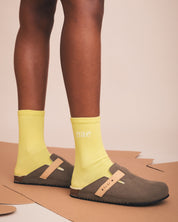 Person wearing yellow socks with 'nae' branding and brown clogs on a beige background