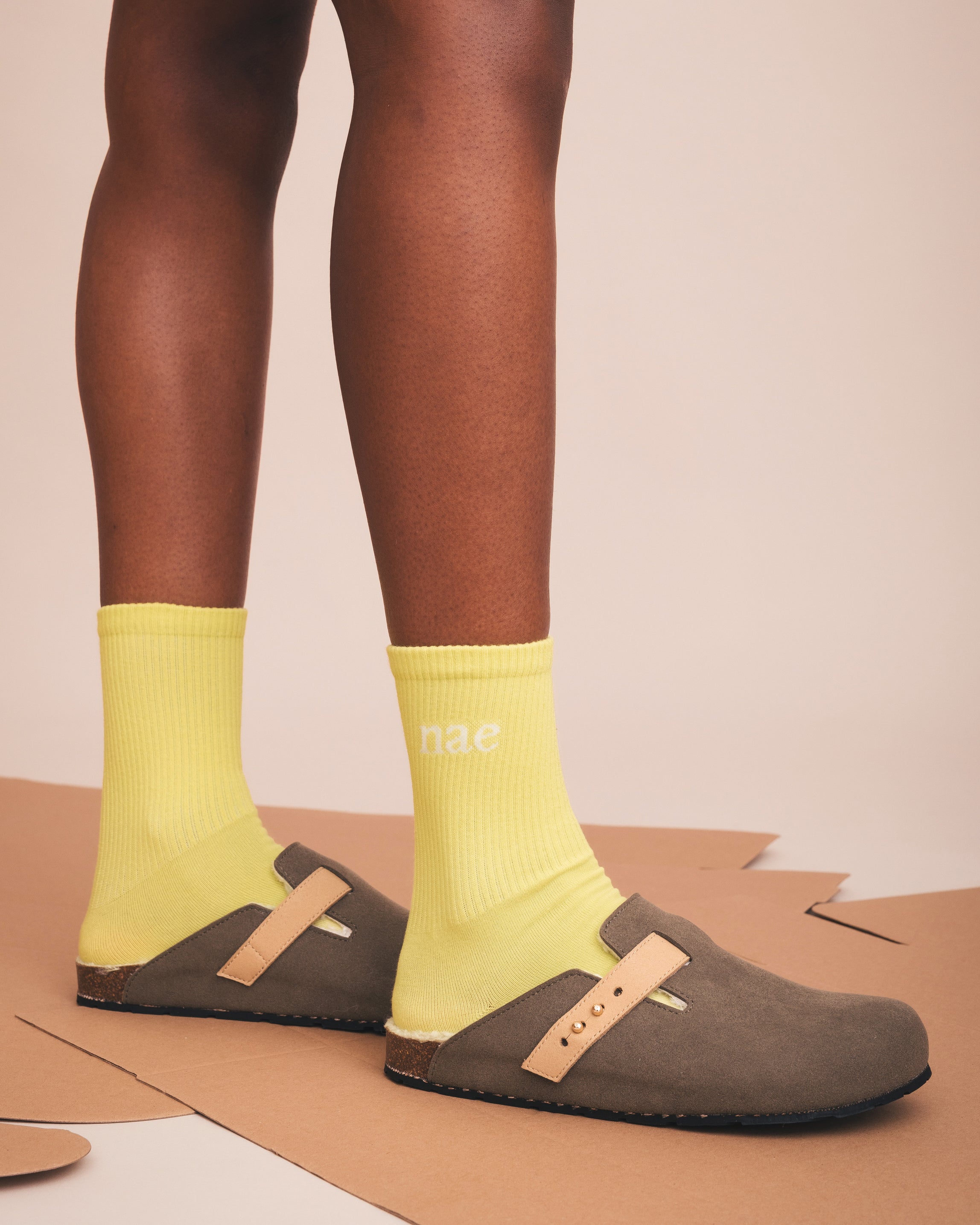 Person wearing yellow socks with 'nae' branding and brown clogs on a beige background