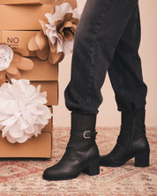 Person wearing black ankle boots with a floral and cardboard box background