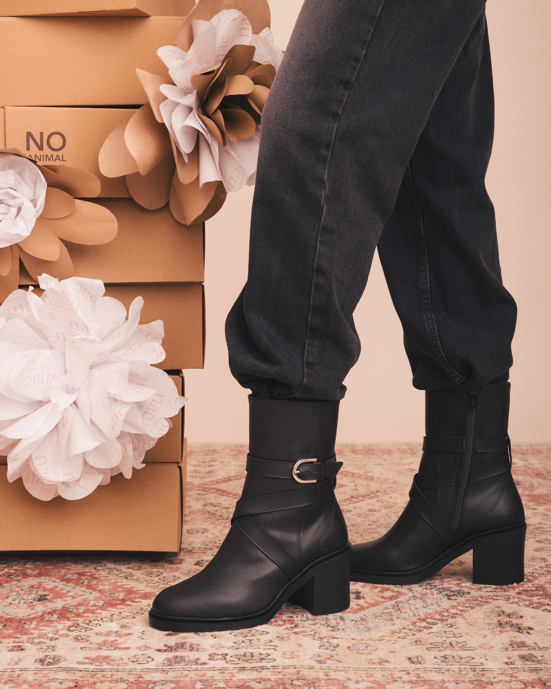 Person wearing black ankle boots with a floral and cardboard box background