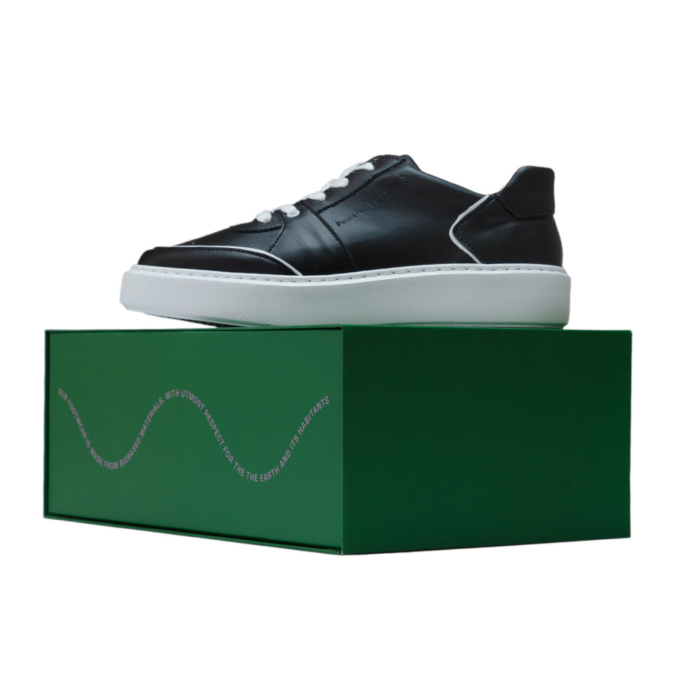 AGAZI EMI Low Black sneakers on a green box, highlighting its sustainable packaging. Sustainability Shoes. Environment friendly shoes.