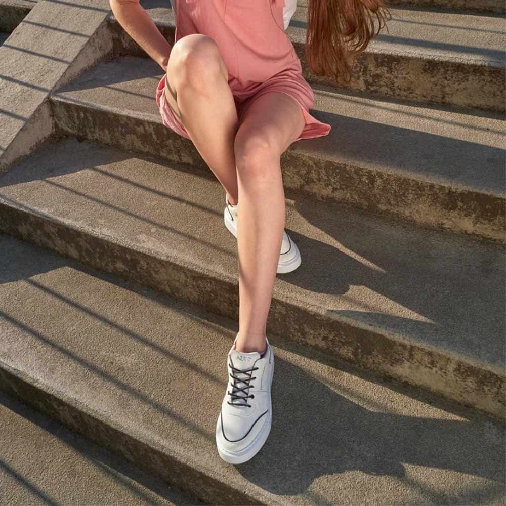 Model wearing Agazi EMI Low Off-White sustainability shoes sitting on steps. Environment friendly shoes paired with a casual outfit, perfect for sustainable fashion enthusiasts.