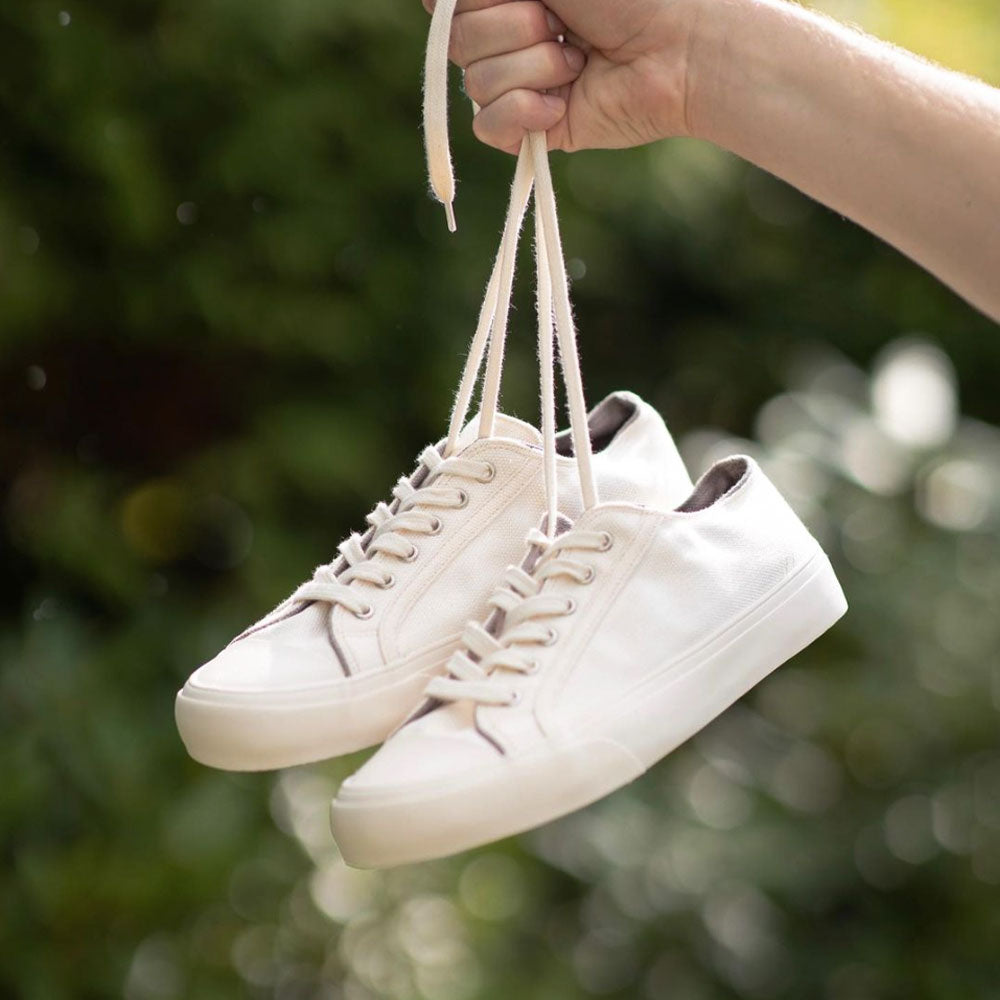 Hand holding a pair of Bamburista Low Top GrassHopper White Sand sneakers by their laces. Emphasizing the lightweight and eco-friendly bamboo textile construction, perfect for sustainable fashion lovers.