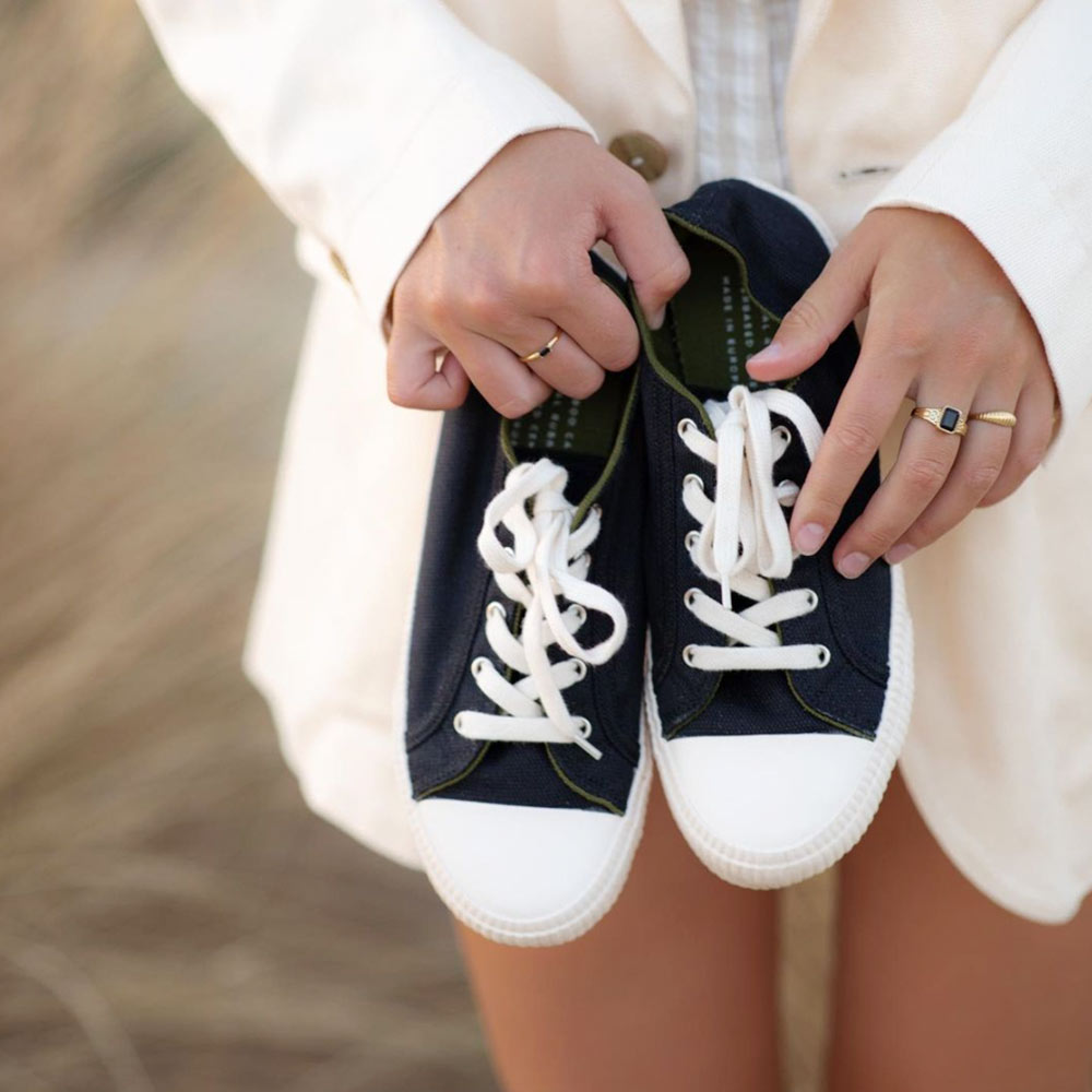 Lifestyle Image - Holding Black Sneakers: A person holding a pair of black Bamburista sneakers, showcasing the stylish and eco-friendly design. The bamboo fiber textile and sustainable shoe materials are highlighted.