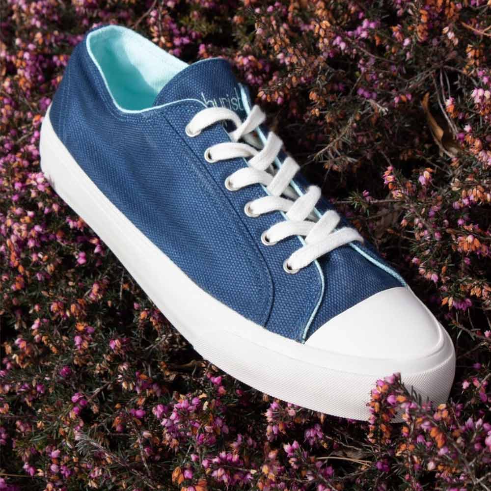 Bamburista Blue sneaker on flowers: A women's blue sneaker made from bamboo fiber textile, laced up, and placed on a bed of purple flowers.