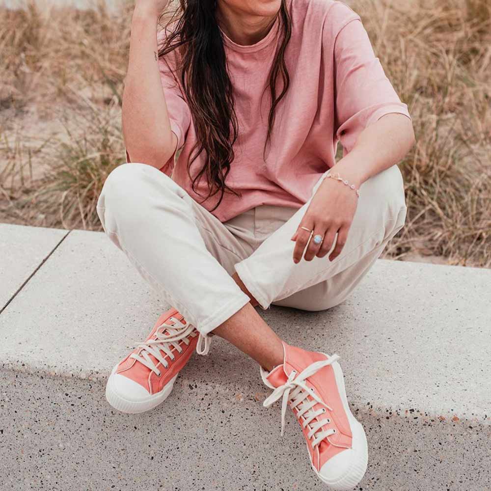 A woman sitting on a concrete ledge, sporting Bamburista Flamingo sneakers made from bamboo textile, highlighting the stylish and sustainable design.