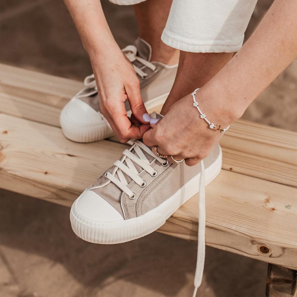 A close-up of a person tying the laces of the Bamburista Grey sneaker, highlighting the use of sustainable bamboo textile and the shoe's eco-friendly features.