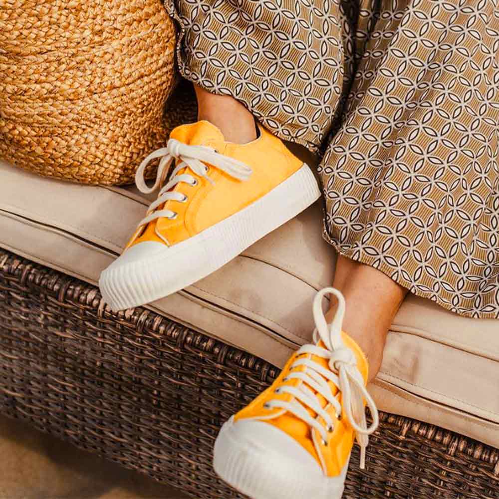 Person wearing Bamburista yellow sneakers, seated on a cushion, showcasing the sustainable shoe in a casual setting.