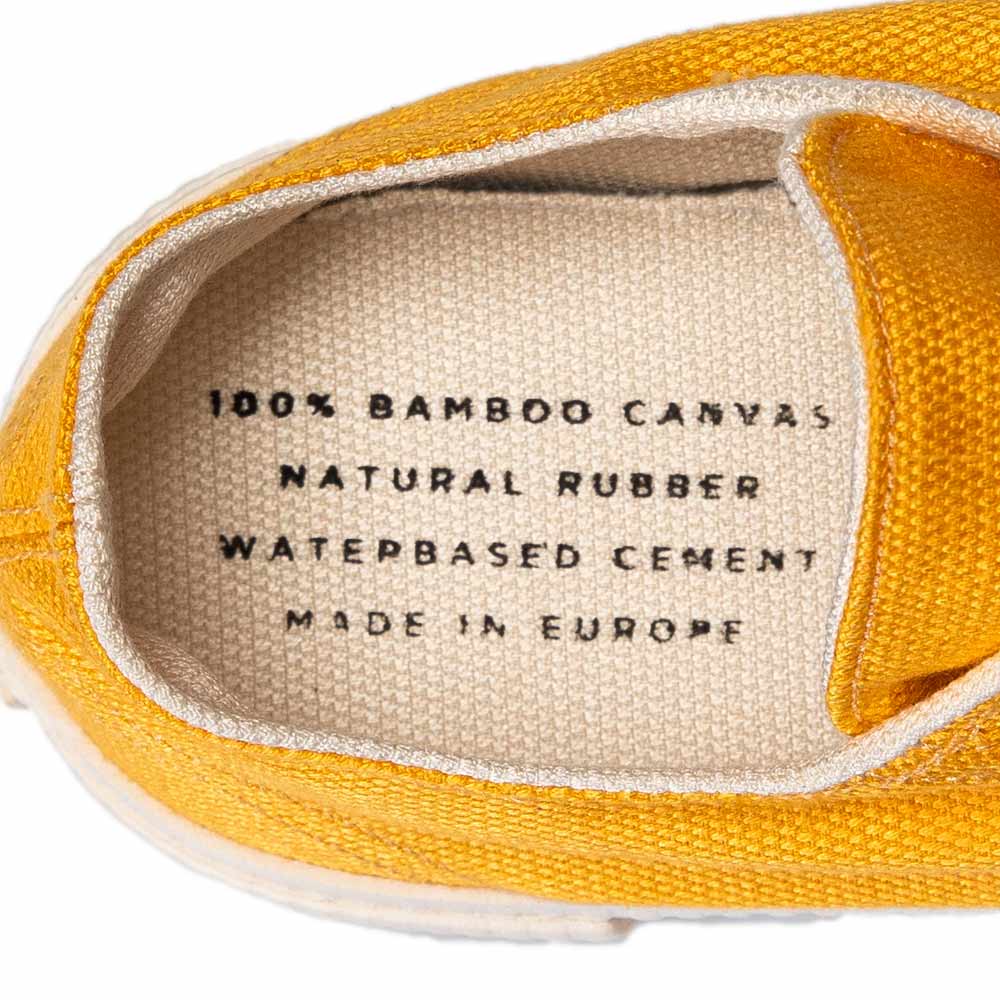 Close-up of the inside of a Bamburista yellow sneaker, showing the text "100% Bamboo Canvas, Natural Rubber, Waterbased Cement, Made in Europe."