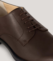 Vegan Derby - Woman close-up showing an elegant brown leather shoe with open lacing system for versatile occasions.