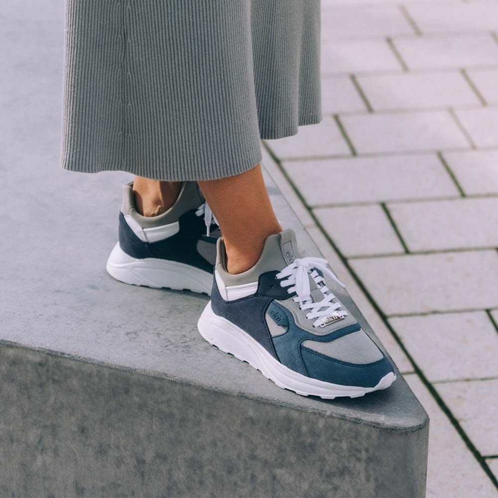 Model wearing Larch Blue Vegan ekn shoes with a grey skirt, standing on a ledge. Showcasing shoes sustainable qualities, perfect for fashion-forward, eco-conscious individuals.