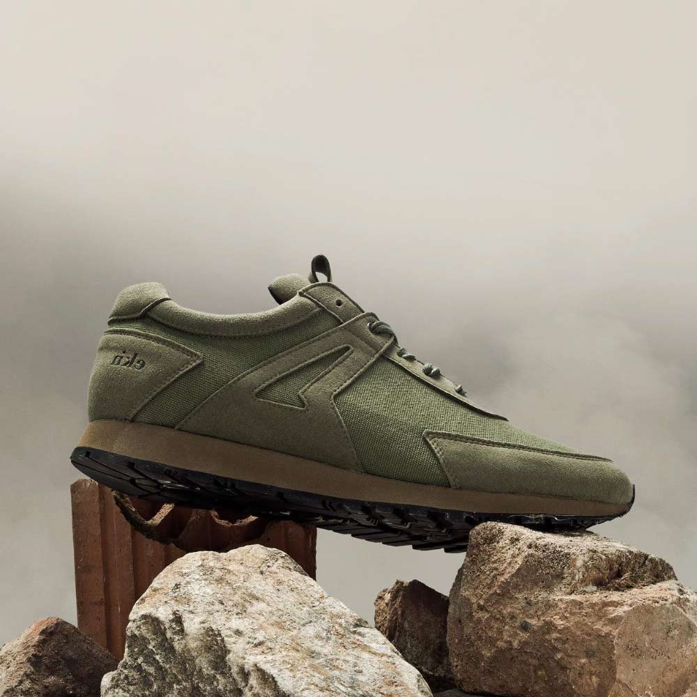 Sustainable shoe, EKN low seed runner color artichoke, outdoor shot is laying on rocks. 