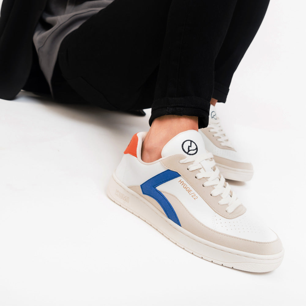 Person wearing KUMI recycled material shoes in white with blue and orange details, Hygge/22 model, showcasing eco-friendly fashion.