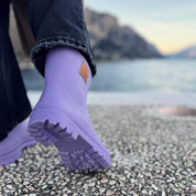 Close-up of a person wearing Thies Bio Rain Boots in lavender near a waterfront, highlighting the vegan boots' sole.