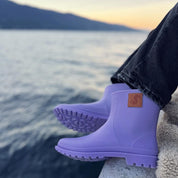 Person wearing Thies Bio Rain Boots in lavender, seated by a lake, emphasizing the vegan boots' style and comfort.