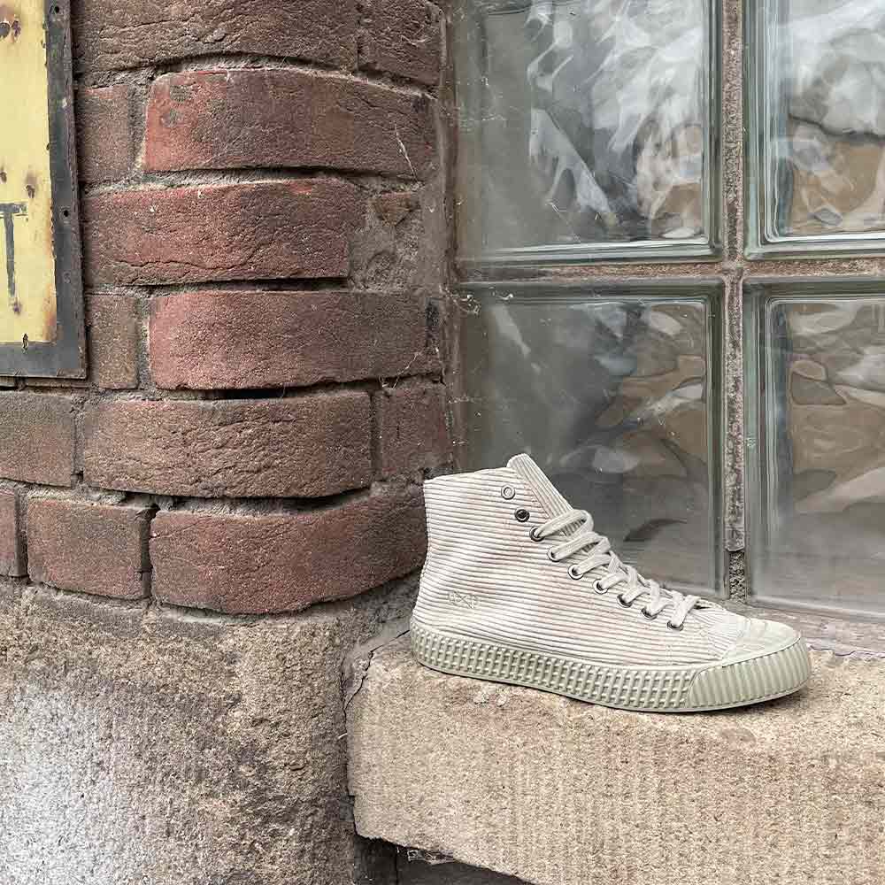 Sustainable shoes by nat2, model Cord Stone, sitting on a window sill, outdoor near a brick wall.